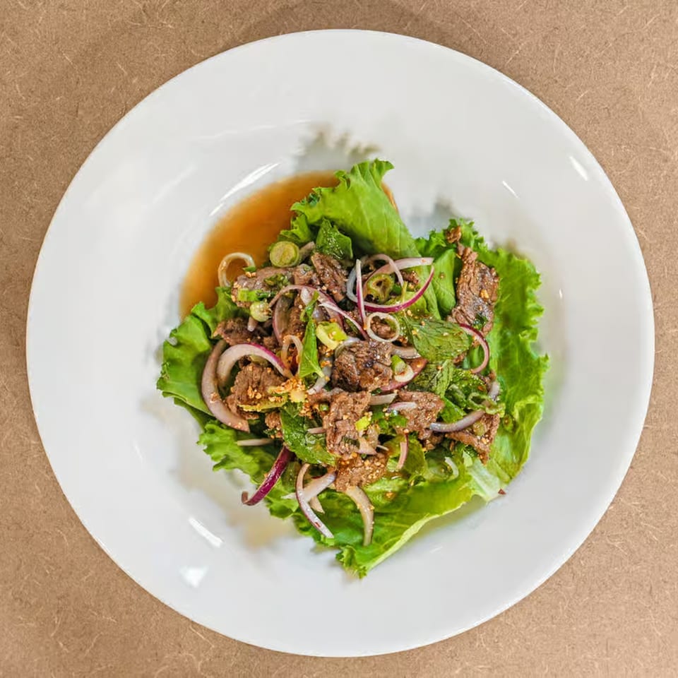 Truly Thai Restaurant's spicy beef salad with red onions, mint, and lettuce on a white plate.