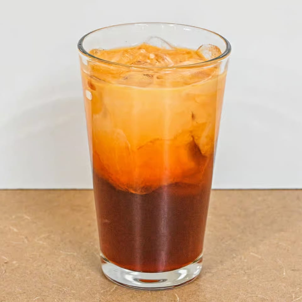 A tall glass of iced Thai tea with distinct layers of dark tea and creamy orange milk.