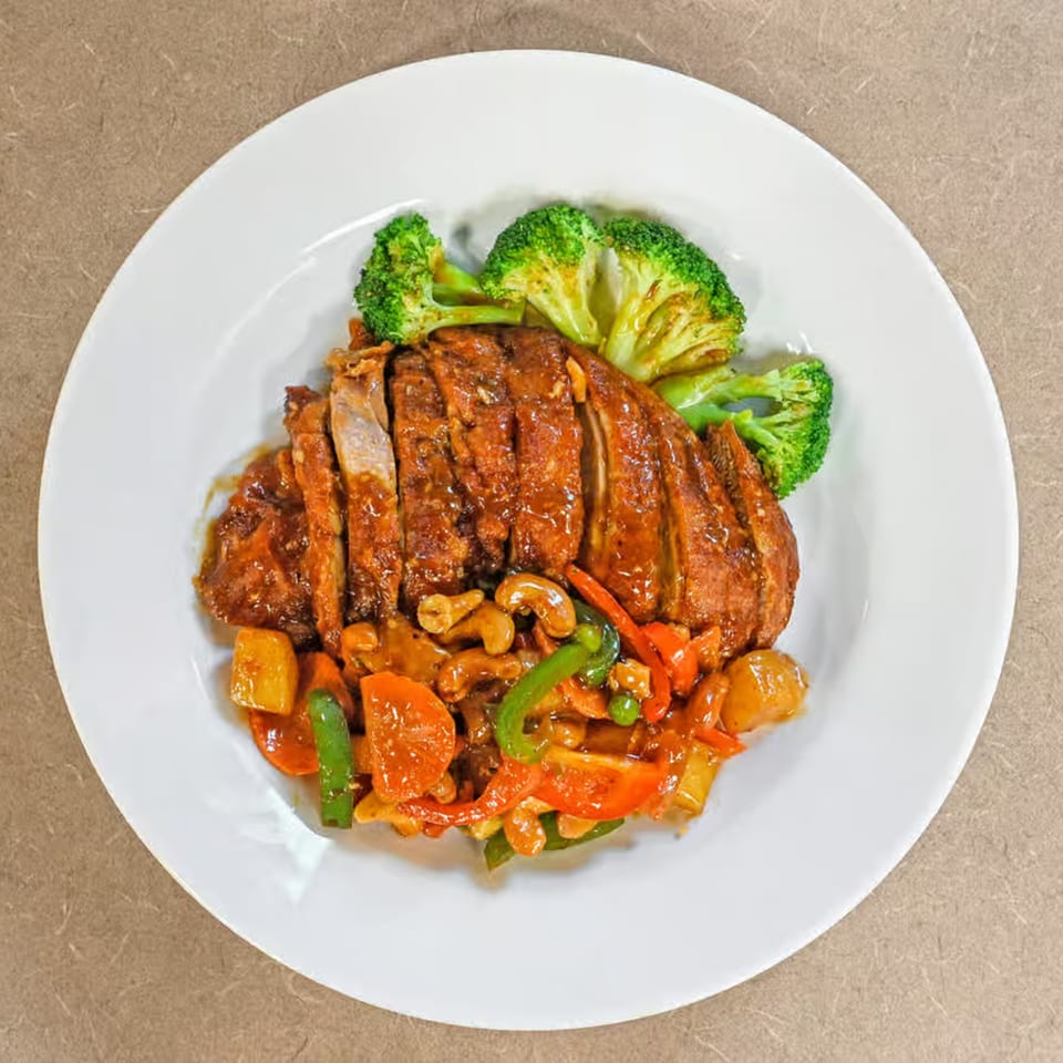 Sliced roasted duck with stir-fried vegetables, cashews, and broccoli on a white plate.